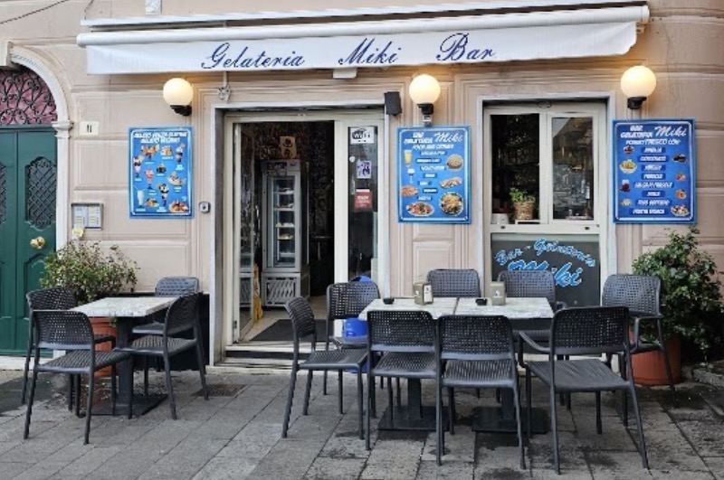 La facciata di Gelateria Miki Bar con la tenda bianca, i menu blu alle pareti e i tavolini all’aperto in Via Tommaso Bottaro